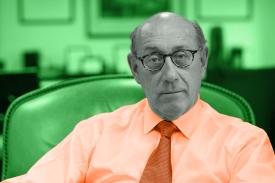 Picture of Kenneth Feinberg sitting in a chair. Green background, orange shirt, black and white face.